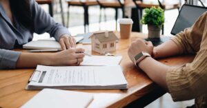 A young couple stands with a home inspector in a kitchen, reviewing a clipboard together.